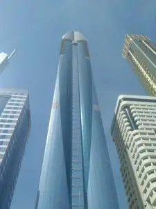 Rose Rayhaan by Rotana hotel tower in Dubai photographed from below, featuring reflective blue glass architecture against a bright clear sky on Sheikh Zayed Road.