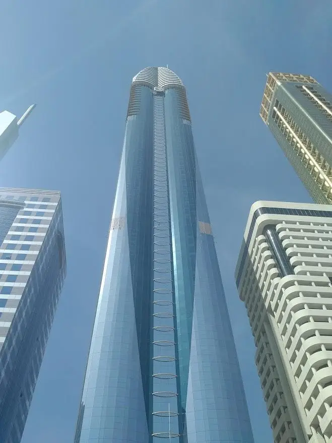 Rose Rayhaan by Rotana hotel tower in Dubai photographed from below, featuring reflective blue glass architecture against a bright clear sky on Sheikh Zayed Road.